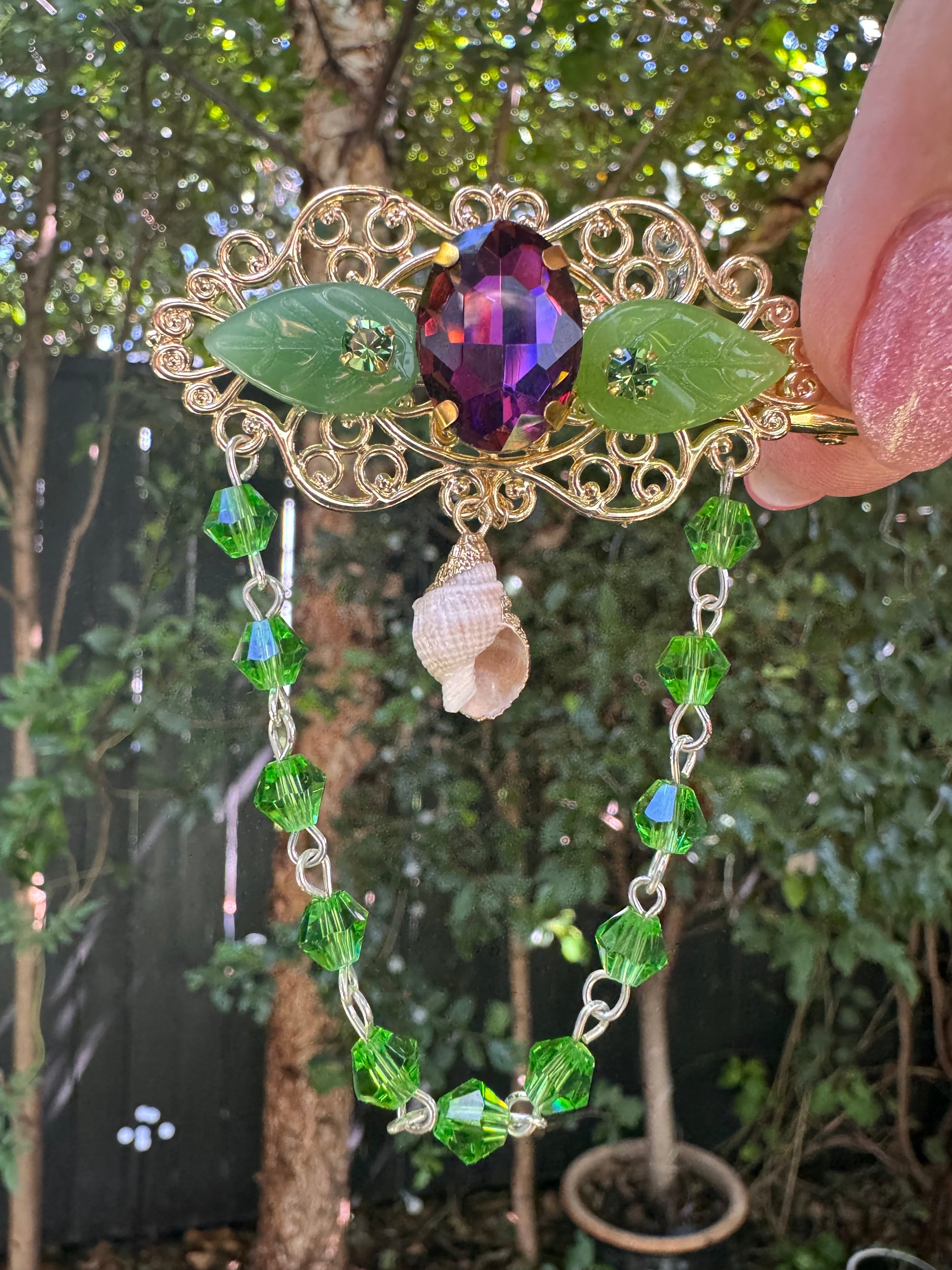 Decorative hair clip with gemstones and green beads held against a natural background