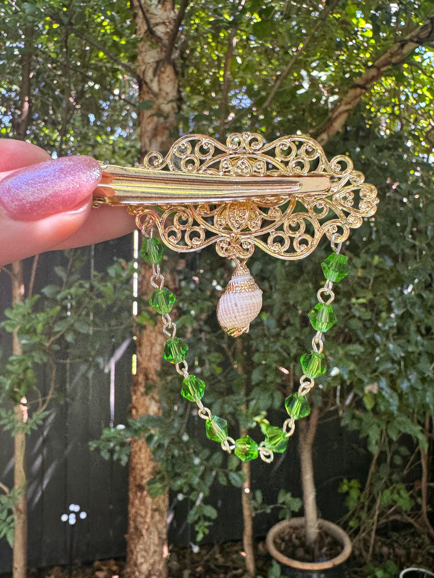 Gold hair clip with green beads held by a hand against a blurred natural background