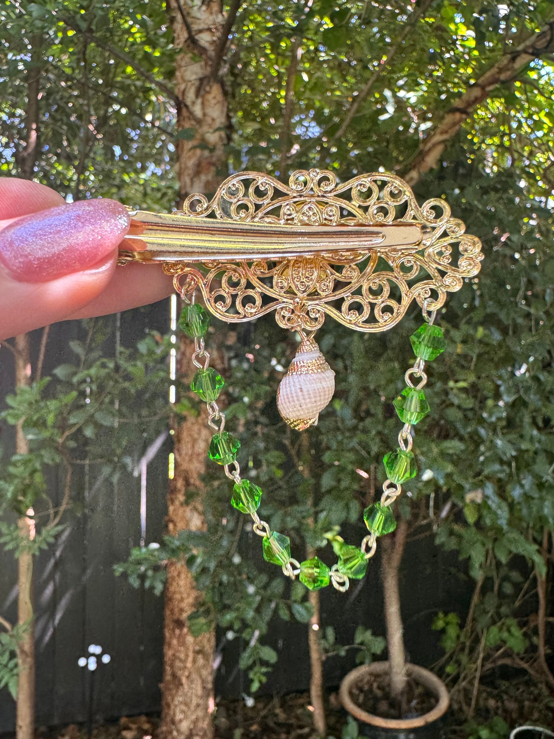 Gold hair clip with green beads held by a hand against a blurred natural background