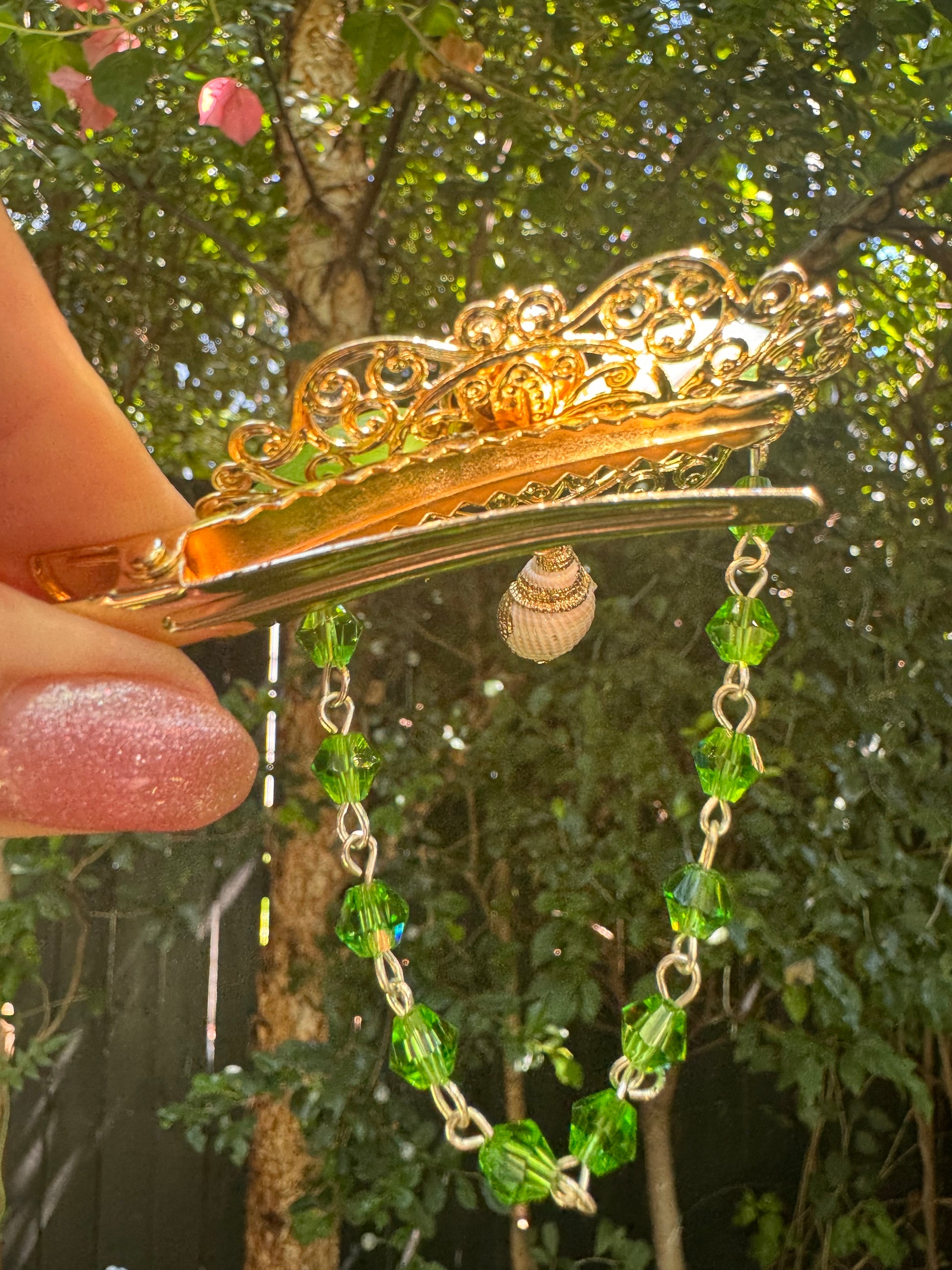 Gold hair clip with green beads held in front of a blurred natural background