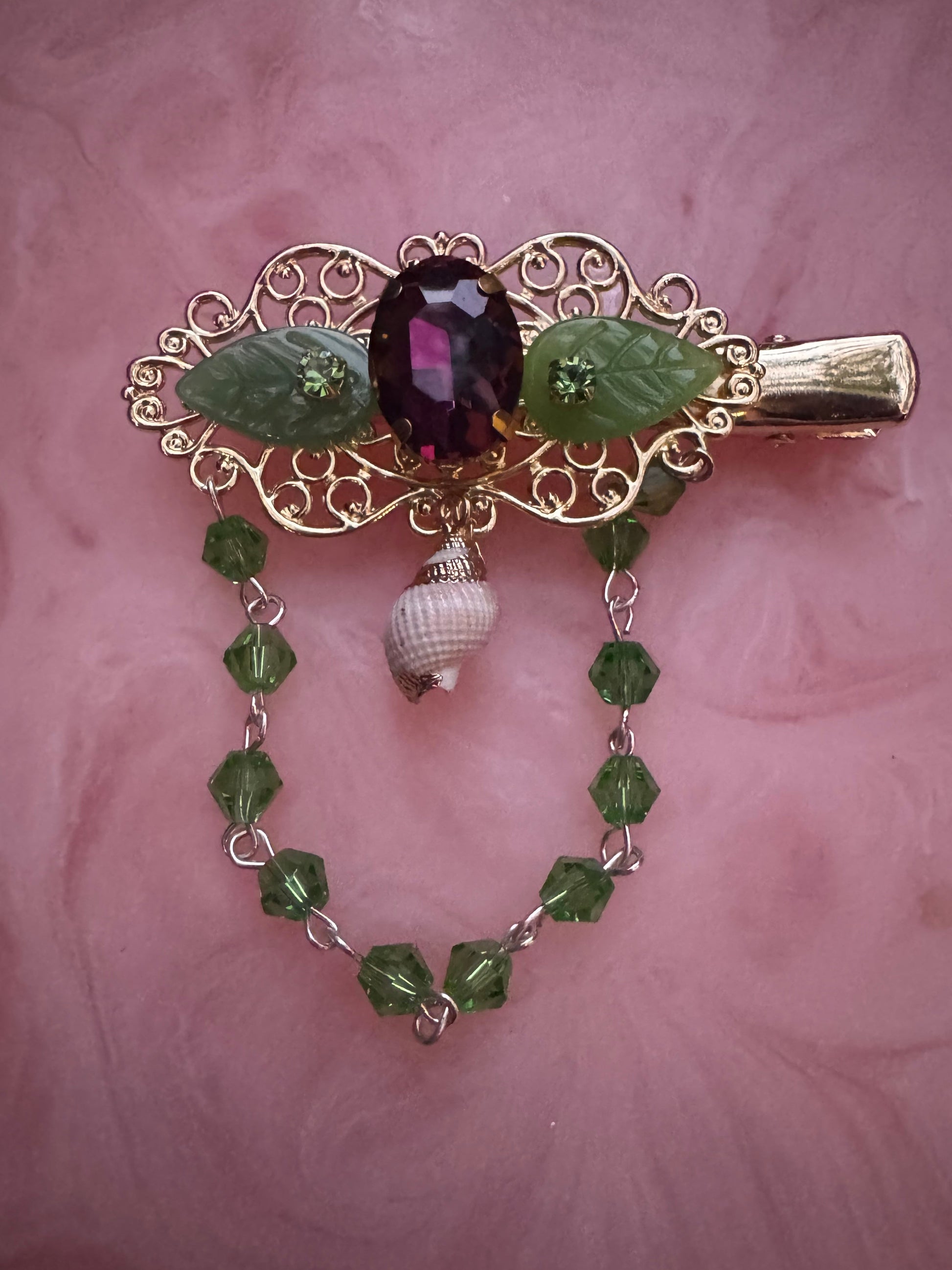 Decorative hair clip with gemstones and leaf design on a pink background