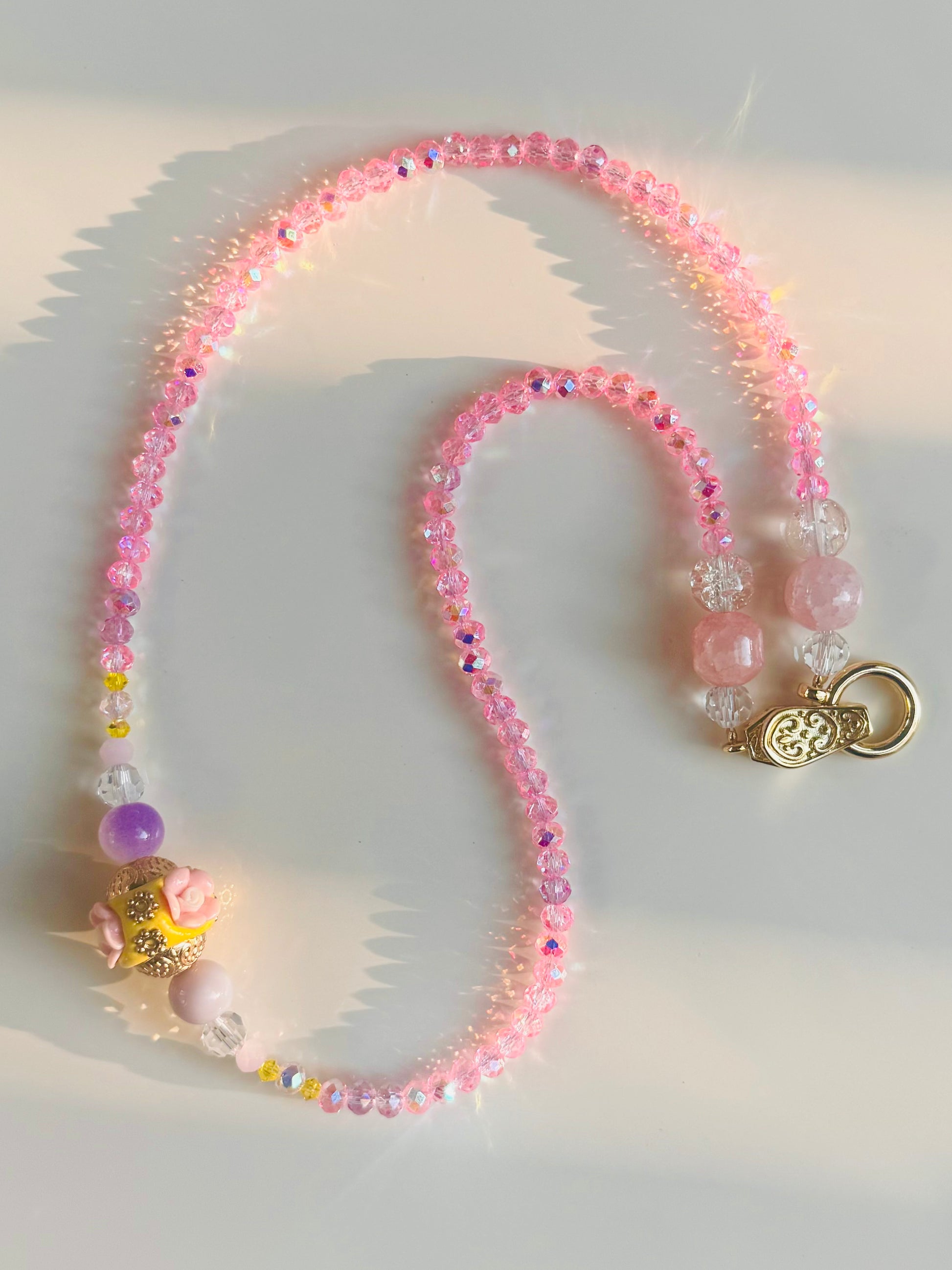 Pink beaded necklace with a gold clasp on a light background