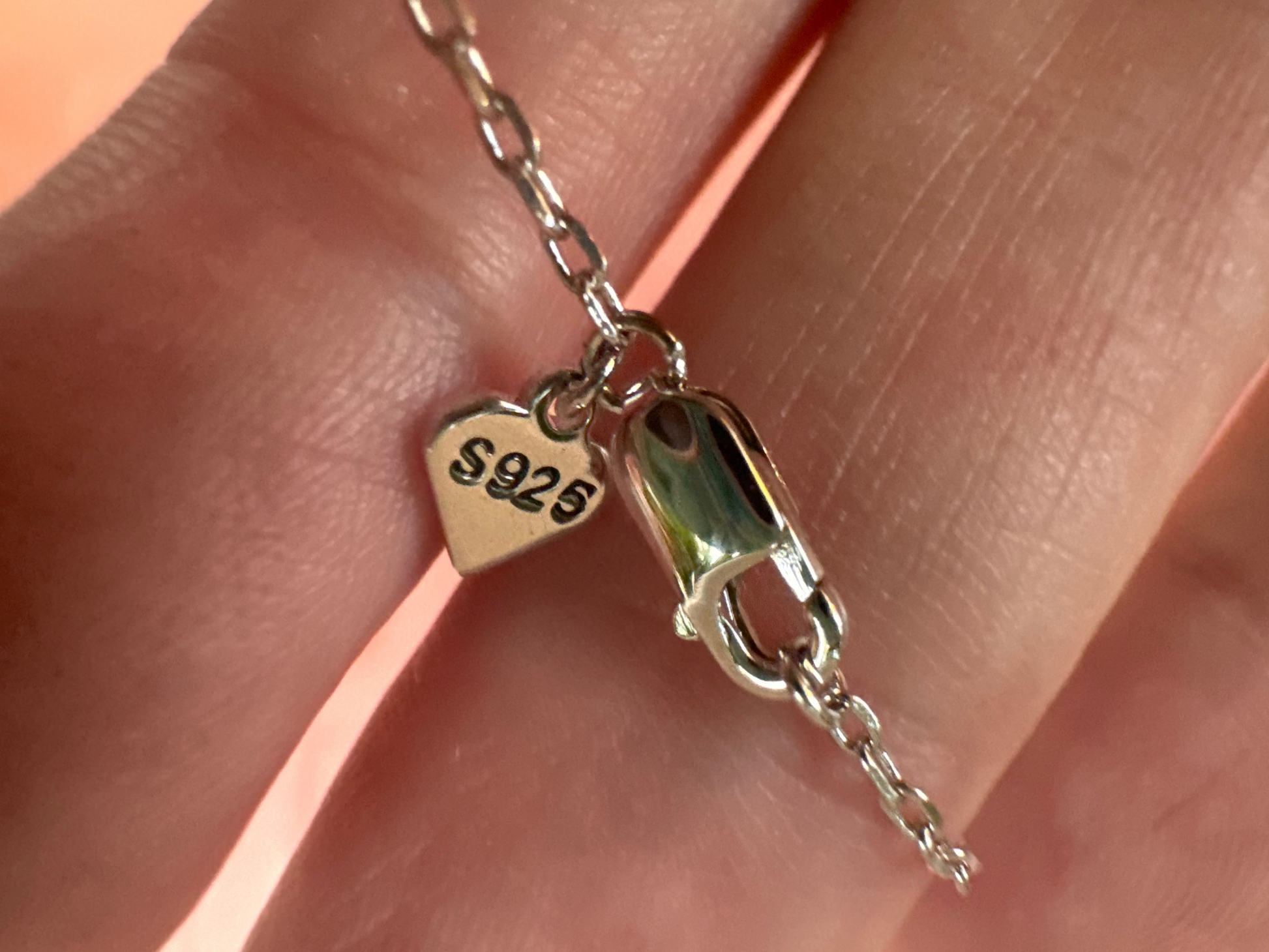 Silver clasp on a chain held between fingers with '925' stamp