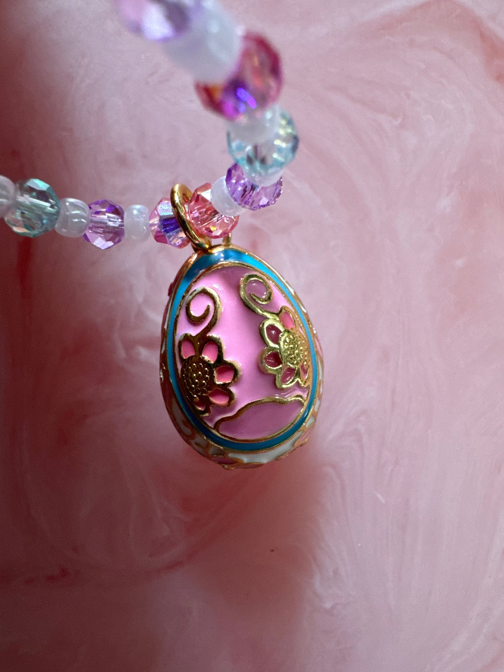 Close-up of a decorative pendant with colorful beads on a pink background