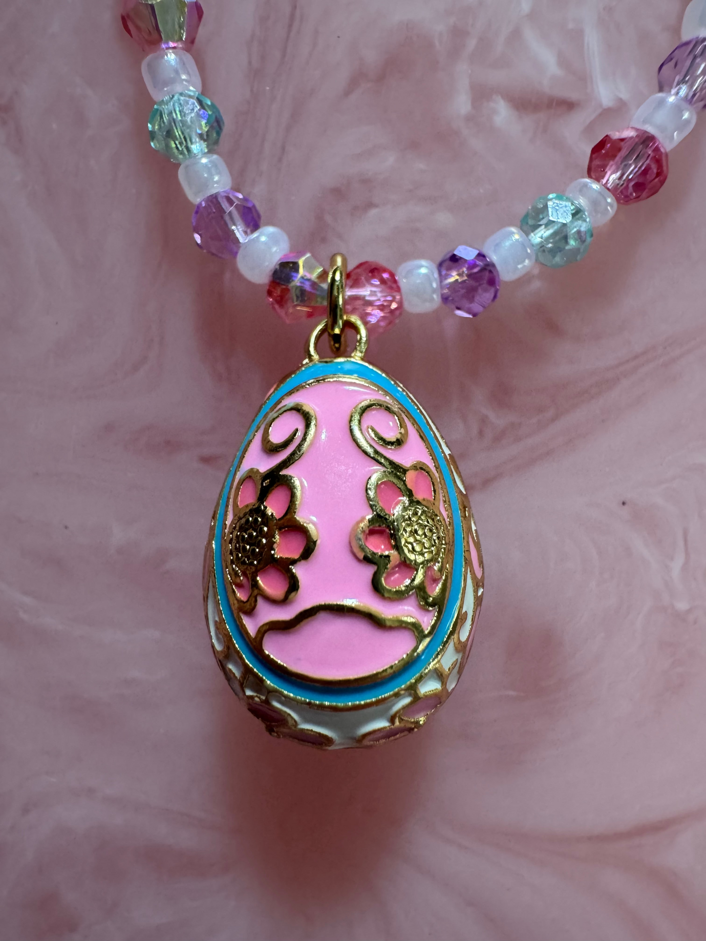 Decorative egg-shaped pendant with a beaded chain on a pink background