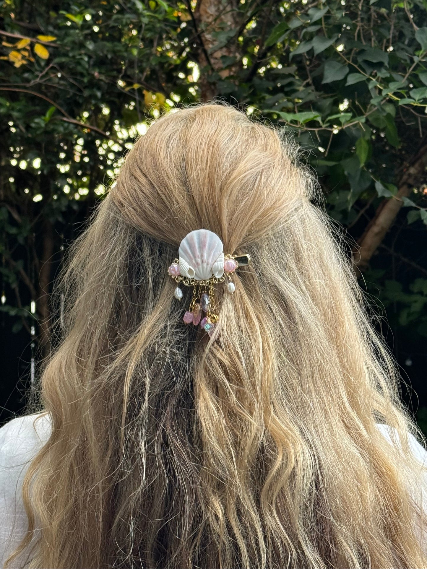 Person with long blonde hair wearing a shell hair accessory in a natural setting