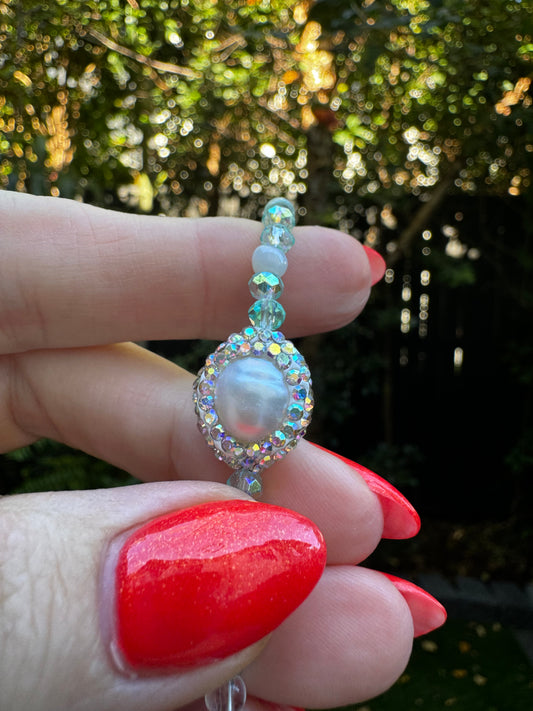Hand holding a beaded ring with a pearl-like center against a blurred natural background