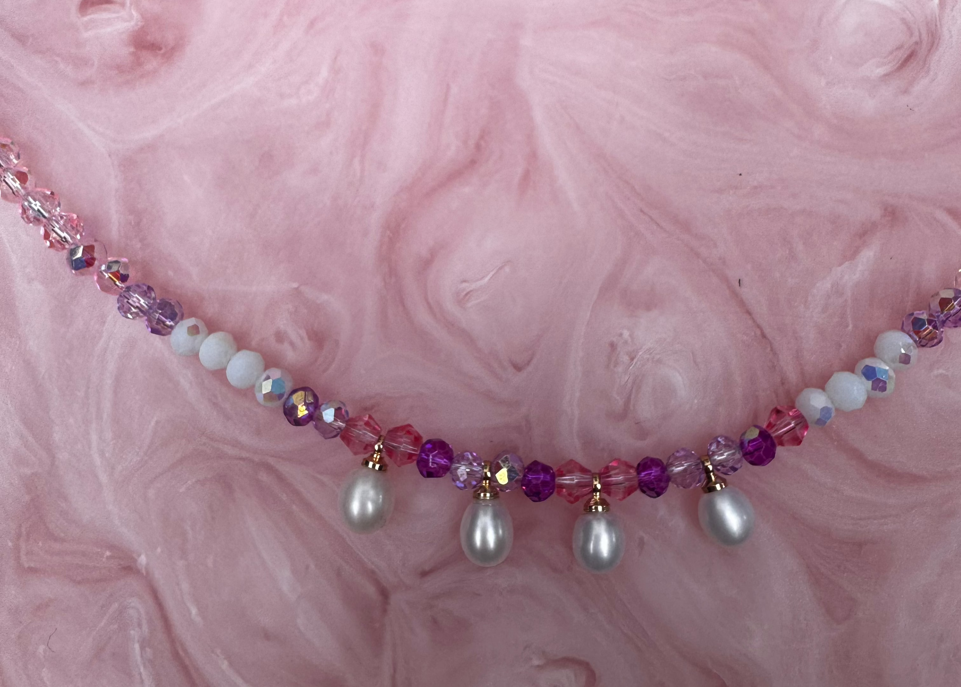 Necklace with beads and pearls on a pink textured background
