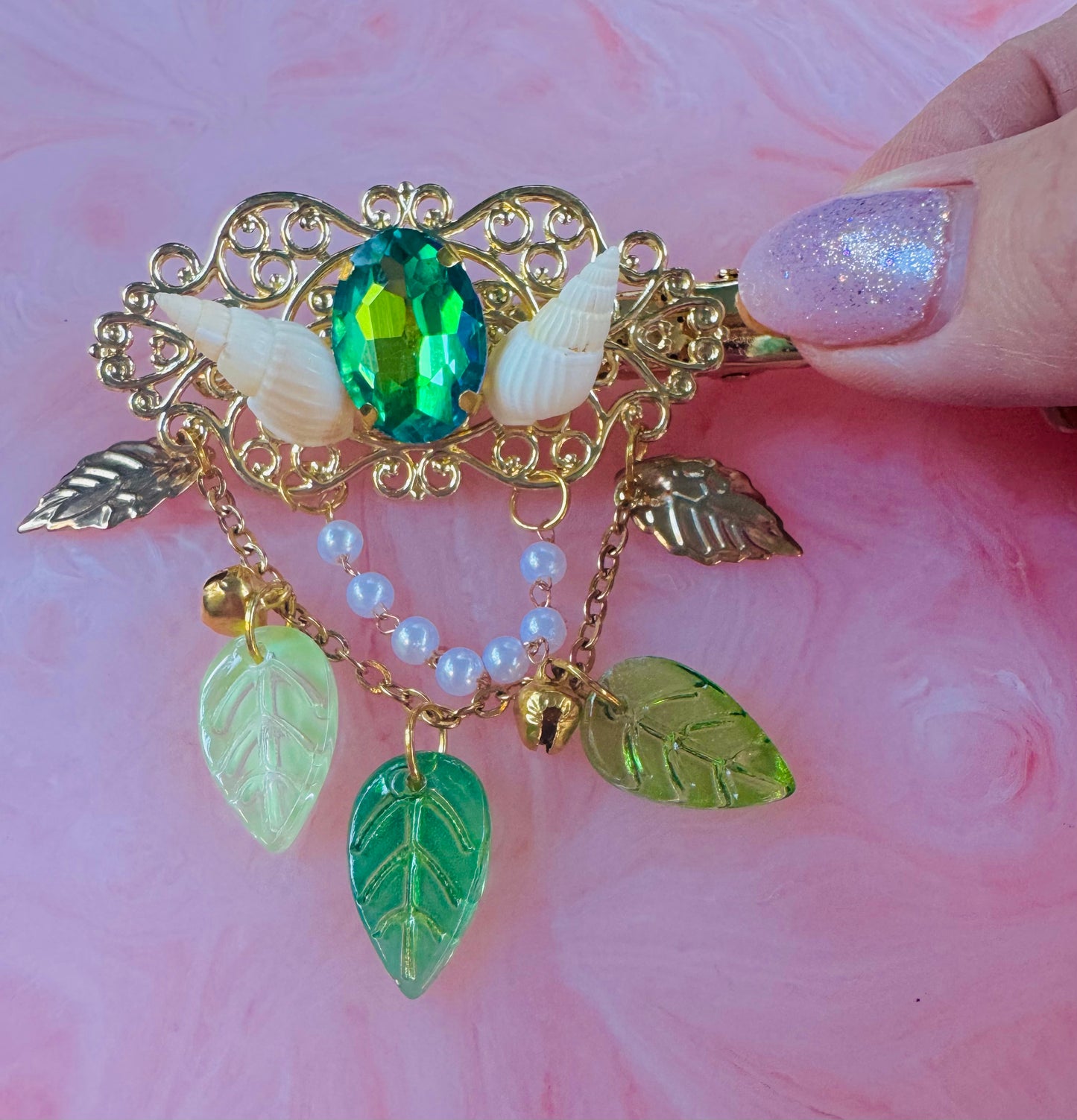 Decorative brooch with green gem, leaves, and pearls on a pink background
