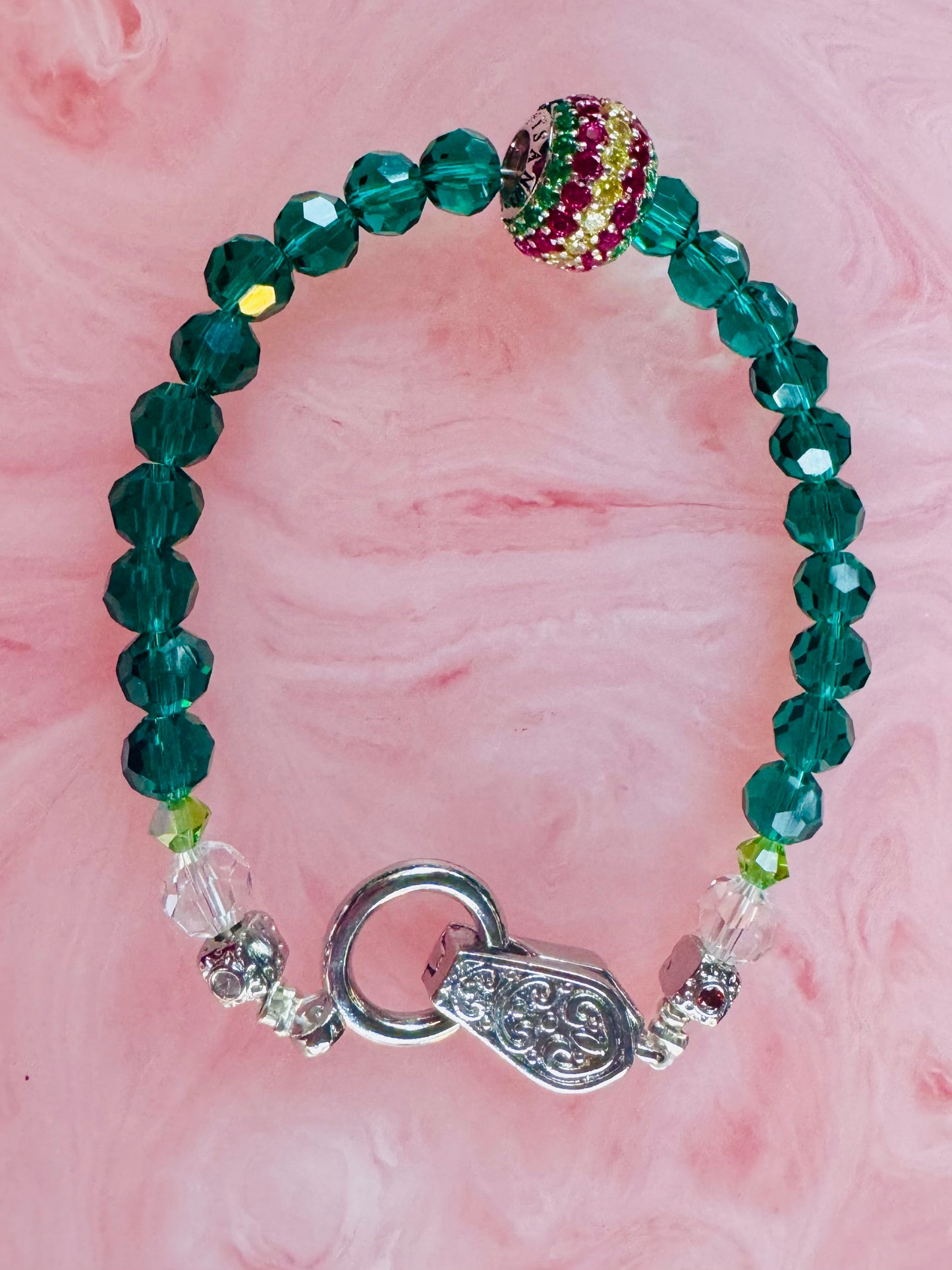 Green beaded bracelet with a silver clasp on a pink background