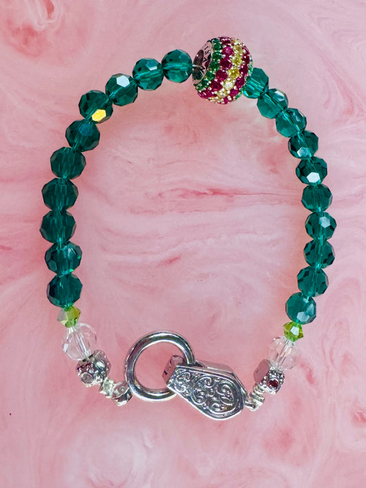 Green beaded bracelet with a silver clasp on a pink background