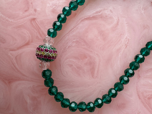 Green beaded necklace with a colorful bead on a pink marble background