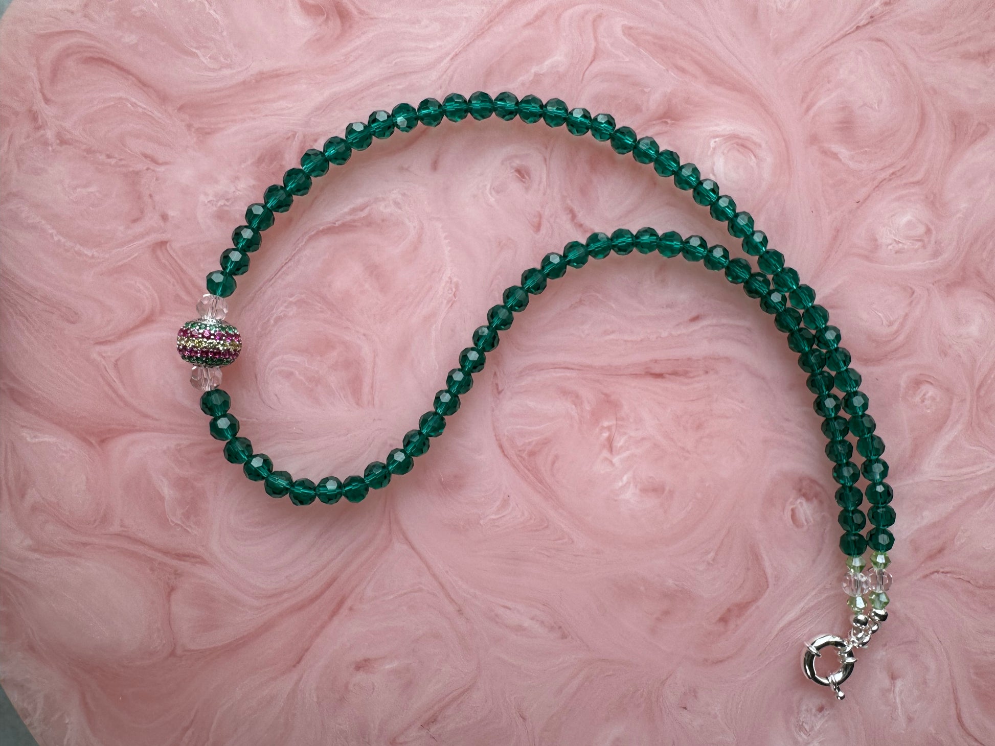 Green beaded necklace with silver clasp on a pink marbled background