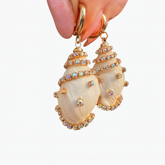 Shell-shaped earrings with gold accents held by a hand against a white background