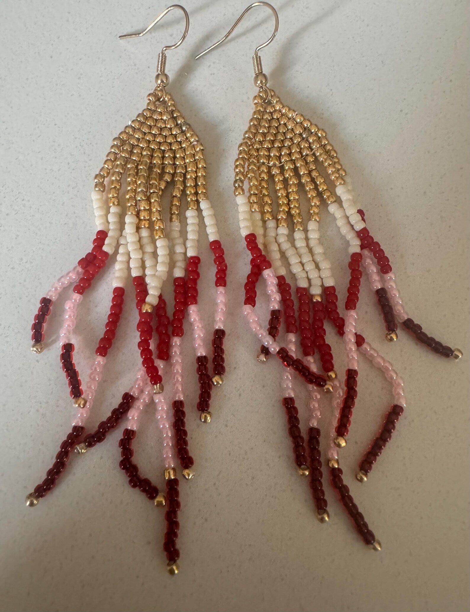 Beaded earrings with gold, red, and white beads on a light background
