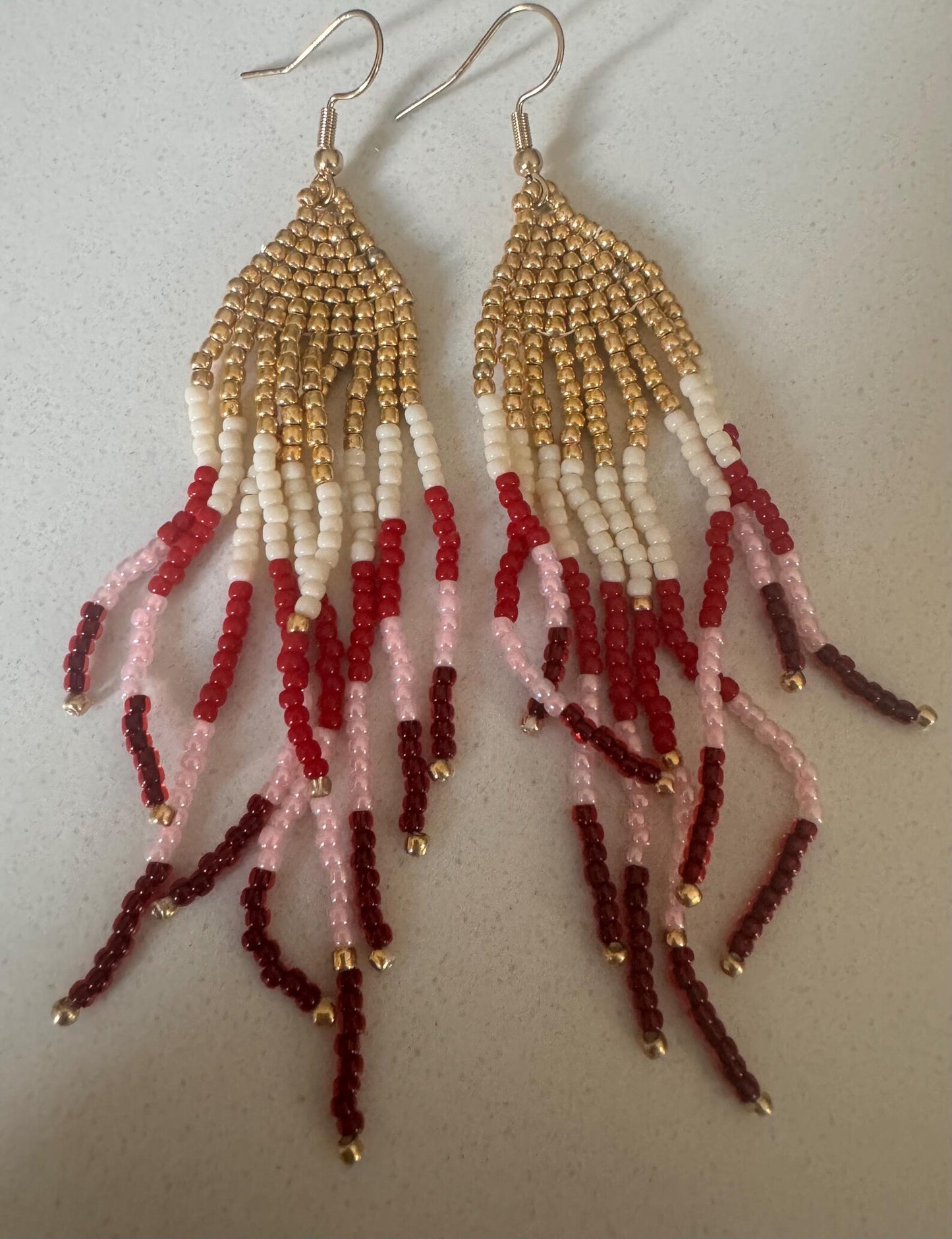Beaded earrings with gold, red, and white beads on a light background